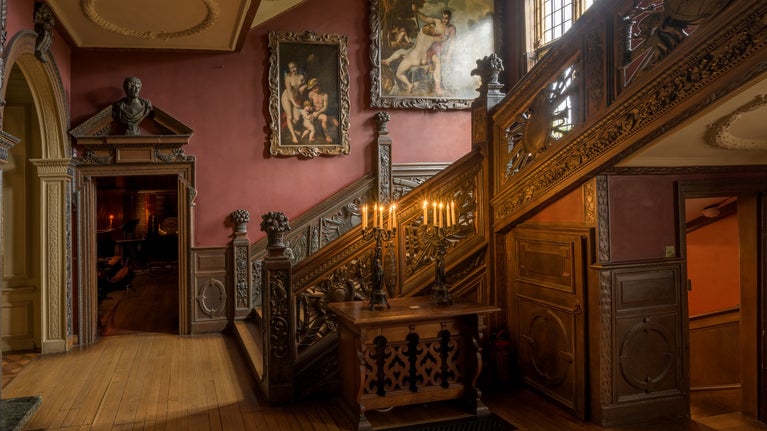 A view of the wooden Great Stairs with red walls above and a doorway into the Chapel at Ham House and Garden, London